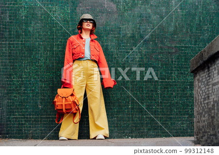 Hipster young woman in bright clothes, sun glasses, backpack bag and bucket hat posing on the green tile wall background. Urban city street fashion. Fashion blogger. Selective focus. Copy space 99312148