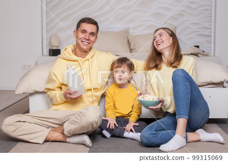 Cute adorable smiling parents with child son sitting by the bed and eating popcorn 99315069