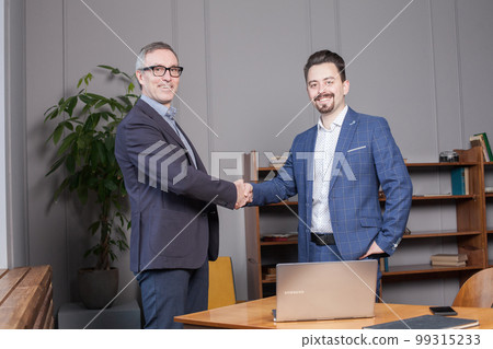 Two happy cherrful businessman in suit making handshake in office, business succes concept 99315233