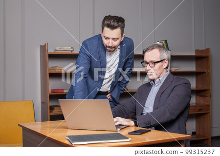 Mature businessman in blue suit and his younger colleague are working on the laptop 99315237