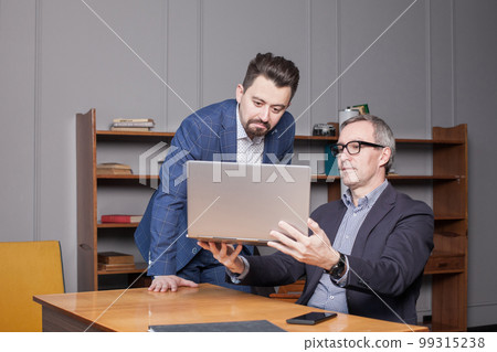 Pensive mature businessman in blue suit is showing new project to his serious partner in office 99315238