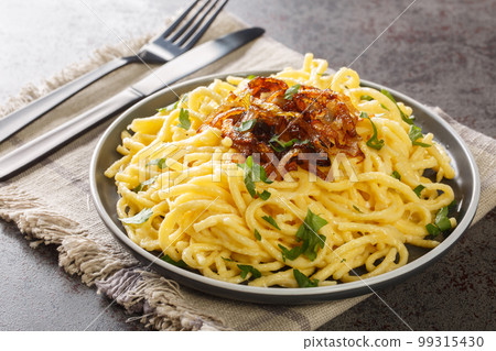 Hot spatzle noodles and grated cheese Emmentaler topped with fried onions closeup on the plate. Horizontal 99315430