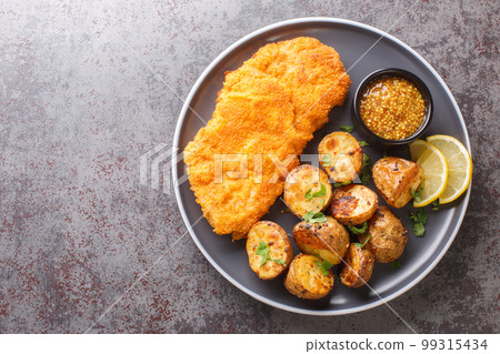 Homemade Munich veal schnitzel fried in breadcrumbs with mustard and horseradish garnished with baked potatoes close-up in a plate. horizontal top view Homemade Munich veal schnitzel fried in breadcrumbs with mustard and horseradish garnished with baked potatoes close-up in a plate. horizontal top view 99315434