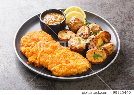 Homemade Munich veal schnitzel fried in breadcrumbs with mustard and horseradish garnished with baked potatoes close-up in a plate. horizontal Homemade Munich veal schnitzel fried in breadcrumbs with mustard and horseradish garnished with baked potatoes close-up in a plate. horizontal 99315440