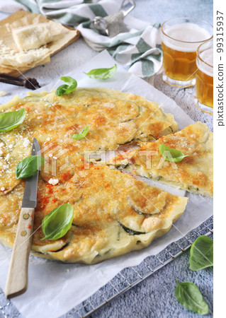 Schiacciatina di zucchini.  Italian cuisine. Thin zucchini salty pie with Parmesan cheese, basil dressing and two glasses of beer 99315937