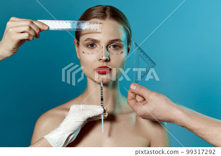 Plastic surgery or face lifting for young woman. Doctor's hands wearing gloves drawing lines, holding head of female patient. Making beauty, modifying face to make surgical correction 99317292