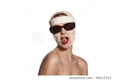 Female face bandaged with medical bandages and sunglasses with human emotions. Making beauty, modifying face to make surgical correction, plastic surgery. correction of asymmetry. 99317331