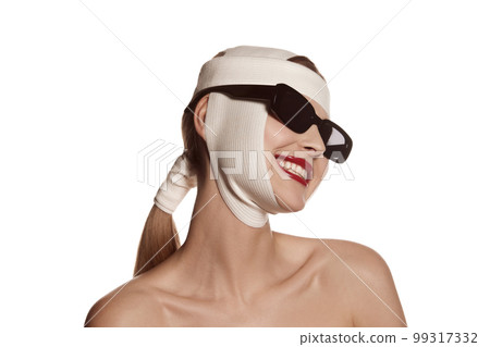 Female face bandaged with medical bandages and sunglasses with human emotions. Making beauty, modifying face to make surgical correction, plastic surgery. correction of asymmetry. 99317332