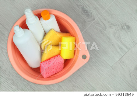 Detergent bottles with washcloths in a pink basin on a wooden background. Top view. Copy space. 99318649