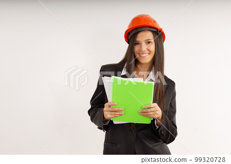 Portrait of happy young woman-architect-designer in business suit and orange helmet with documents in her hands on isolated white. Attractive brunette girl is working on construction project. Portrait of happy young woman-architect-designer in business suit and orange helmet with documents in her hands on isolated white. Attractive brunette girl is working on construction project. 99320728