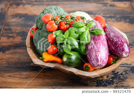 Fresh organic vegetables in wooden bowl. Broccoli, eggplant, zucchini, cherry tomatoes and bell pepper on a wooden table. 99321470