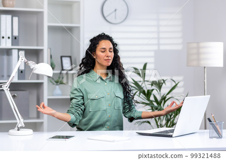Young beautiful hispanic woman relaxing in home office, successful businesswoman meditating in lotus position sitting at workplace with laptop, freelancer in green shirt in living room. 99321488