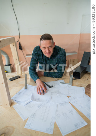 Portrait of a carpenter in a plaid shirt draws a workshop blueprint. Portrait of a carpenter in a plaid shirt draws a workshop blueprint. 99322190