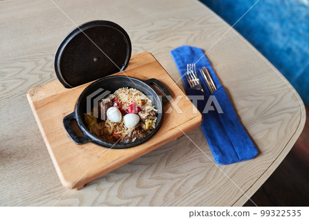 Pilaf on a platter with beef on a wooden background with appliances. The concept of Oriental cuisine. Homemade Uzbek beef pilaf is served in cast-iron dishes. Space for copying. High quality photo Pilaf on a platter with beef on a wooden background with appliances. The concept of Oriental cuisine. Homemade Uzbek beef pilaf is served in cast-iron dishes. Space for copying. High quality photo 99322535