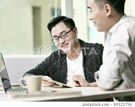 two young asian entrepreneurs discussing business in office using digital tablet and laptop computer 99322756