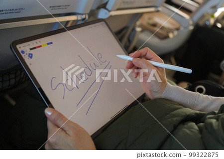 A person operating a tablet on an airplane, writing letters on a memo app 99322875