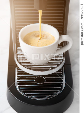 Pouring fresh morning coffee from home espresso machine to white cup on white. 99322891