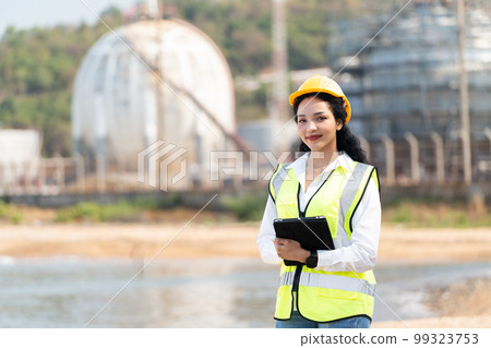 female engineer with hardhat with petrochemical factory background. asian woman holding tablet, plan and Walkie Talkie. 99323753