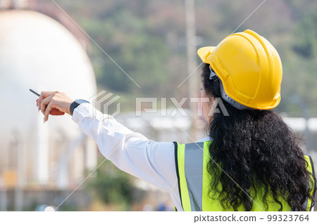 female engineer with hardhat with petrochemical factory background. asian woman holding tablet, plan and Walkie Talkie. 99323764