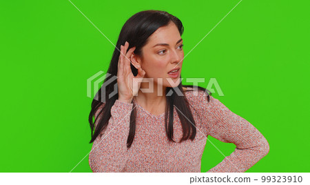 Young woman trying hear you, looking confused and frowning, keeping arm near ear for louder voice 99323910