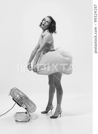 Black and white portrait of young beautiful woman in retro dress standing near fan. Hot summer days 99324197