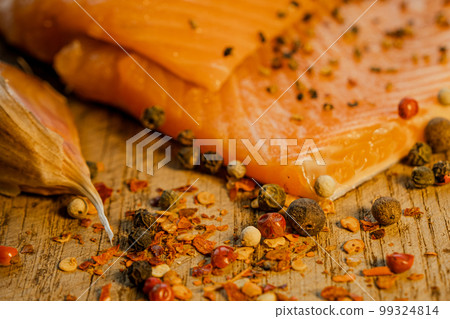 Pieces of fresh juicy trout fillet with spices in the foreground. Trout and garlic in the background. 99324814