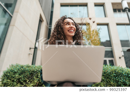 Young woman using laptop while sitting by the building outdoors. Young woman using laptop while sitting by the building outdoors. 99325397