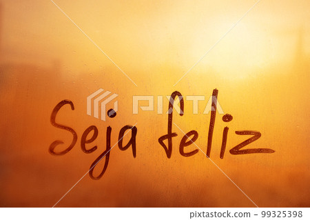 Lettering Portuguese language wish Seja feliz is Be happy in english on foggy glass wet sunset window Lettering Portuguese language wish Seja feliz is Be happy in english on foggy glass wet sunset window 99325398