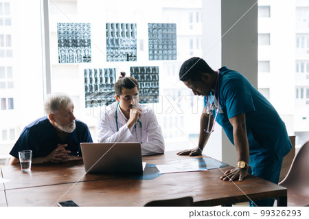 Team of multi-ethnic medical specialists discussing at X-ray image of together during medical conference. on background wall-mounted light box with X-ray and MRI. Concept of medicine and health care. 99326293