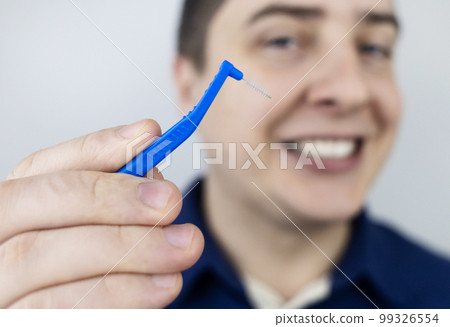Interdental brush. A man shows a brush for cleaning the interdental space. Brush for cleaning teeth and daily oral care. Dentistry and orthodontics  99326554