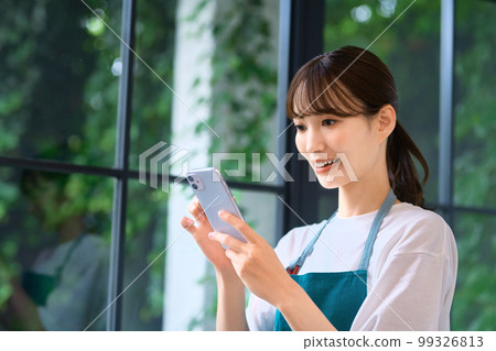 一位穿著圍裙的年輕家庭主婦操作智能手機 99326813