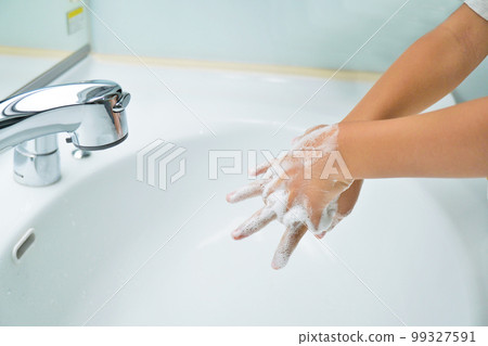 Hands of a toddler scrubbing the palms and fingers with lathered soap in a bright washbasin 99327591