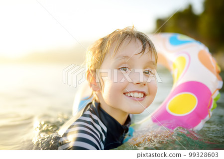 Little boy swimming with colorful floating ring in sea on sunny summer day. Cute child playing in clean water. Family and kids resort holiday during summer vacations. Little boy swimming with colorful floating ring in sea on sunny summer day. Cute child playing in clean water. Family and kids resort holiday during summer vacations. 99328603
