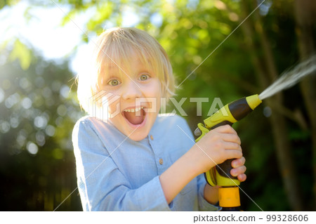 Funny little boy watering plants and playing with garden hose with sprinkler in sunny backyard. Preschooler child having fun with spray of . Summer outdoors activity for kids. 99328606