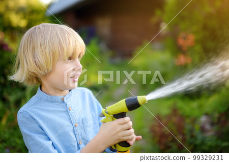 Funny little boy watering plants and playing with garden hose with sprinkler in sunny backyard. Preschooler child having fun with spray of . Summer outdoors activity for kids. 99329231