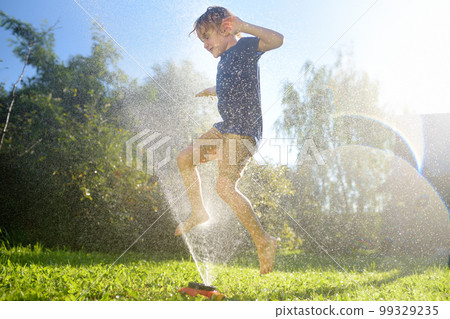 Funny little boy playing with garden sprinkler in sunny backyard. Preschooler child laughing, jumping and having fun with spray of water. Summer holidays for kids in the village Funny little boy playing with garden sprinkler in sunny backyard. Preschooler child laughing, jumping and having fun with spray of water. Summer holidays for kids in the village 99329235