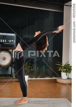 A girl in a black sports uniform does yoga standing on a mat in the gym A girl in a black sports uniform does yoga standing on a mat in the gym 99329308