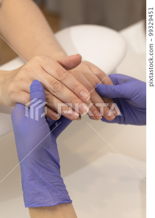 white manicure technician, nail stylist in gloves holds hands of Caucasian client, preparing Japanese eco manicure, polishing in beauty salon. Examining, checking nail condition. Vertical plane 99329451