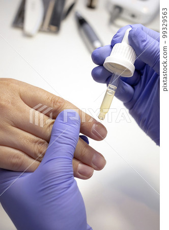 Cropped nail technician applies natural oil on cuticle, fingernails. Eco Japanese bio manicure. Safe organic nail treatment for adults, children, expectant moms. Vertical plane, closeup Cropped nail technician applies natural oil on cuticle, fingernails. Eco Japanese bio manicure. Safe organic nail treatment for adults, children, expectant moms. Vertical plane, closeup 99329563