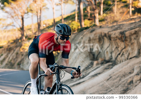 Professional cyclist going down a hill. Athlete in helmet and glasses riding road bike outdoors. Professional cyclist going down a hill. Athlete in helmet and glasses riding road bike outdoors. 99330366