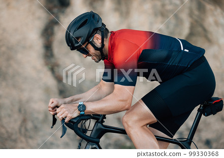 Side view of a cyclist putting effort during training outdoors.Male athlete riding a bicycle. Side view of a cyclist putting effort during training outdoors.Male athlete riding a bicycle. 99330368