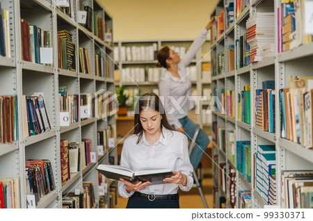 Two young female students in a public library. Two young female students in a public library. 99330371
