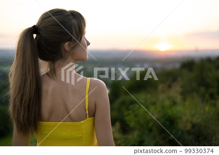 Young woman standing in green field enjoying sunset view in evening nature. Relaxation and meditation concept. Young woman standing in green field enjoying sunset view in evening nature. Relaxation and meditation concept. 99330374