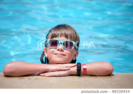Young joyful child girl resting on swimming pool side with clear blue water on sunny summer day. Tropical vacations concept Young joyful child girl resting on swimming pool side with clear blue water on sunny summer day. Tropical vacations concept 99330454