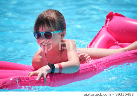 Young child girl falling in water from inflatable air mattress in swimming pool while swinnimg during tropical vacations. Safety of aquatic activities concept Young child girl falling in water from inflatable air mattress in swimming pool while swinnimg during tropical vacations. Safety of aquatic activities concept 99330498