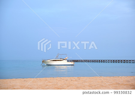 White motor boat floats in ocean water at long pier bridge under bright blue sky, view from sandy beach. Summer traveling concept White motor boat floats in ocean water at long pier bridge under bright blue sky, view from sandy beach. Summer traveling concept 99330832