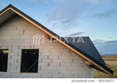 Unfinished house with aerated lightweight concrete walls and wooden roof frame covered with metallic tiles under construction 99330873