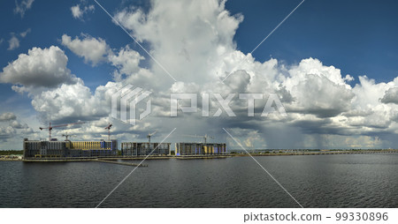 Tower cranes and frame structure of high residential apartment buildings at construction site on sea bay shore. Real estate development at waterfront 99330896