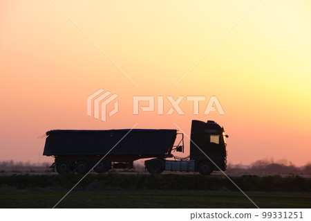 Semi-truck with tipping cargo trailer transporting sand from quarry driving on highway hauling goods in evening. Delivery transportation and logistics concept Semi-truck with tipping cargo trailer transporting sand from quarry driving on highway hauling goods in evening. Delivery transportation and logistics concept 99331251