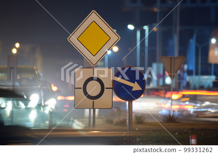 Roundabout road signs with blurred cars on city street traffic at night. Urban transportation concept 99331262